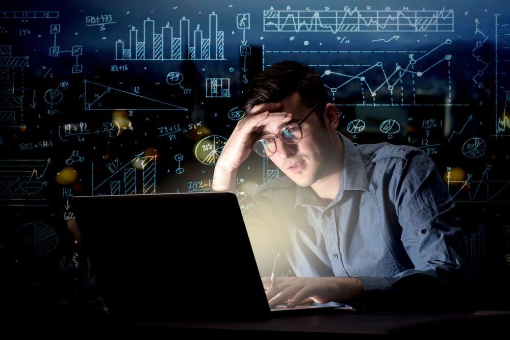 Young handsome businessman working late at night in the office with blue calculations in the background
